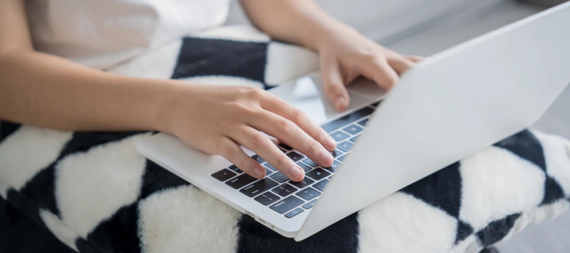 Person using a laptop while seated on a sofa, with hands resting on the keyboard and trackpad.