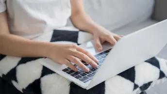 Person using a laptop while seated on a sofa, with hands resting on the keyboard and trackpad.