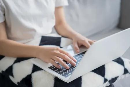 Person using a laptop while seated on a sofa, with hands resting on the keyboard and trackpad.